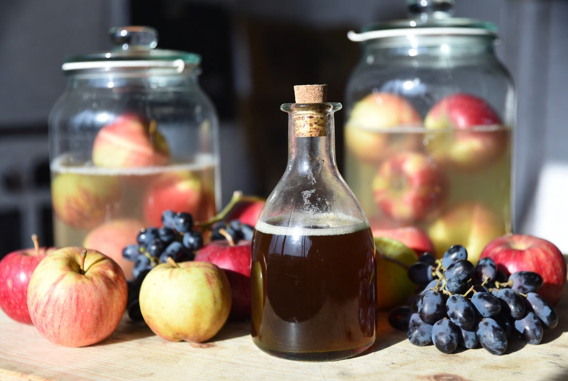 Bottle of homemade vinegar with apples and grapes on wooden table top.