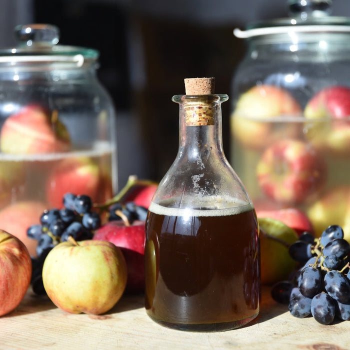 Bottle of homemade vinegar with apples and grapes on wooden table top.