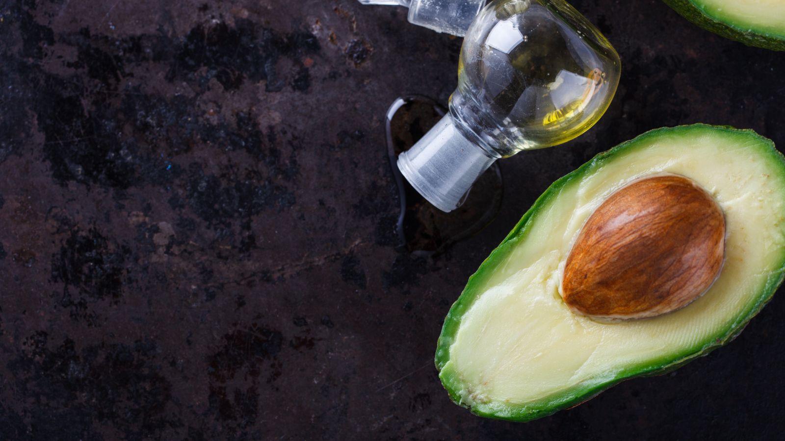 Fresh avocado half with pit beside a glass bottle of avocado oil