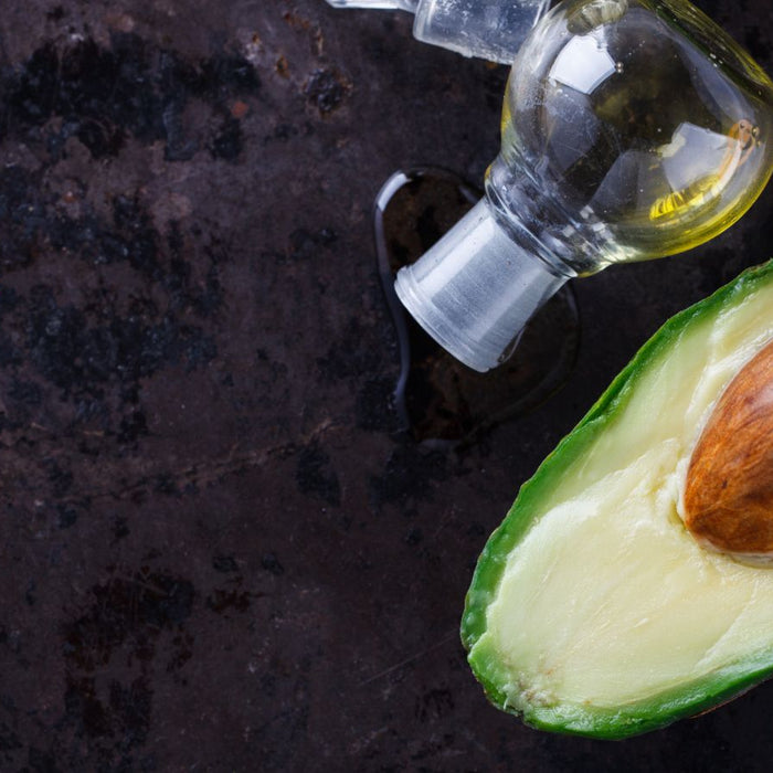 Fresh avocado half with pit beside a glass bottle of avocado oil