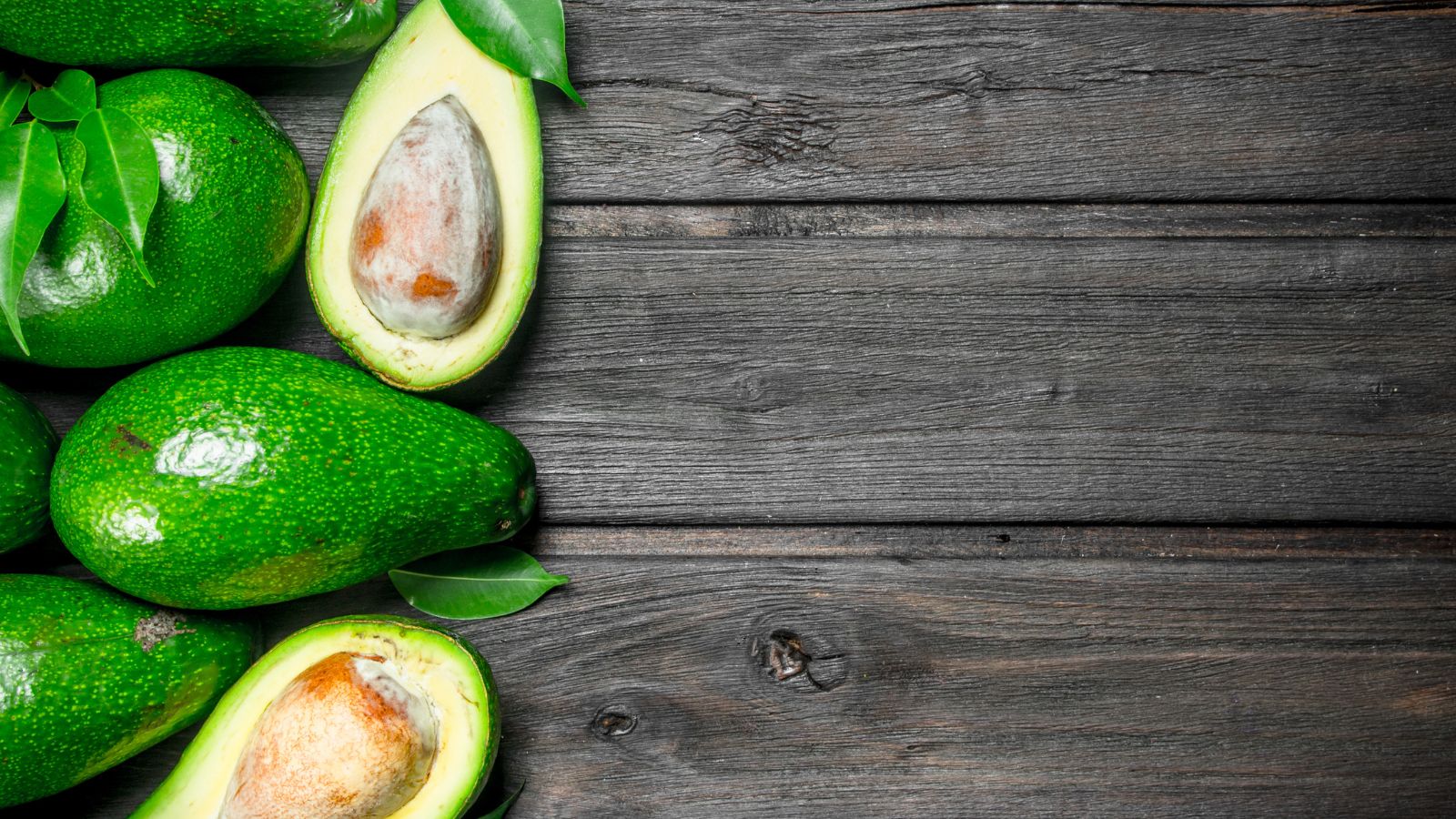 Whole and halved avocados with leaves on rustic wooden table