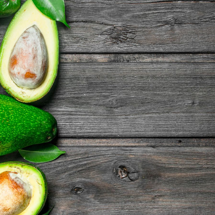 Whole and halved avocados with leaves on rustic wooden table