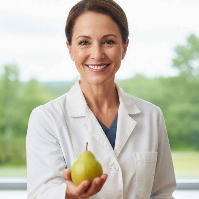Smiling woman in lab coat holding a pear near window