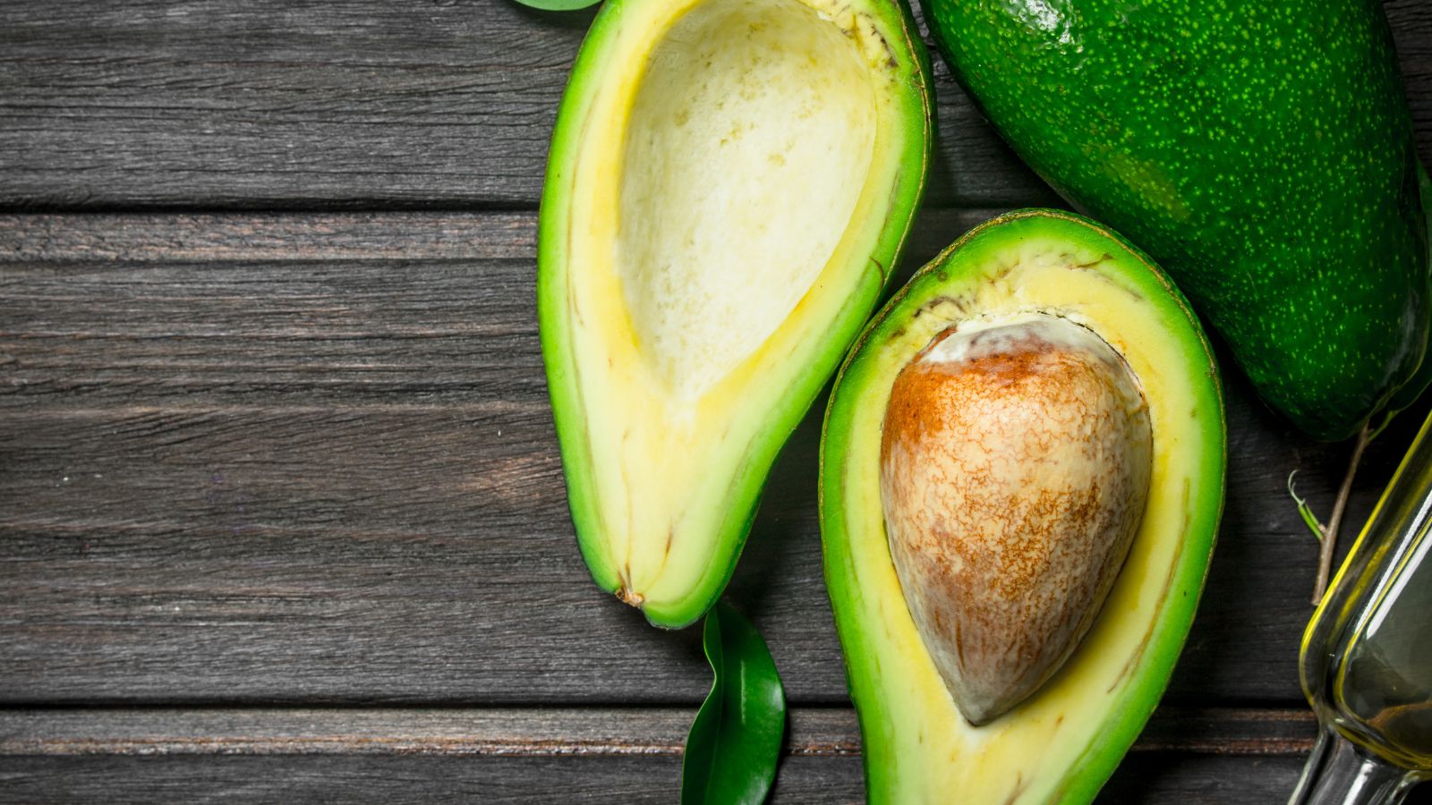 Ripe avocado halves with seed on dark rustic wooden surface