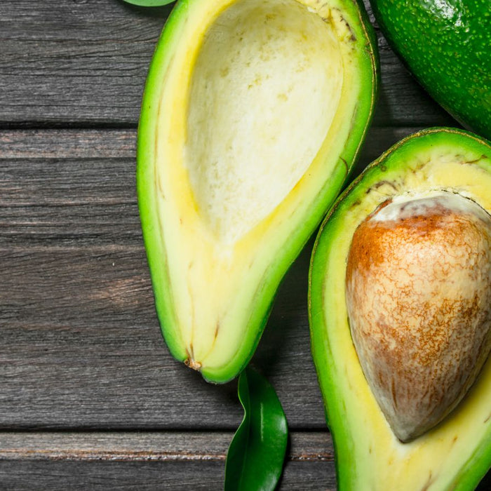 Ripe avocado halves with seed on dark rustic wooden surface