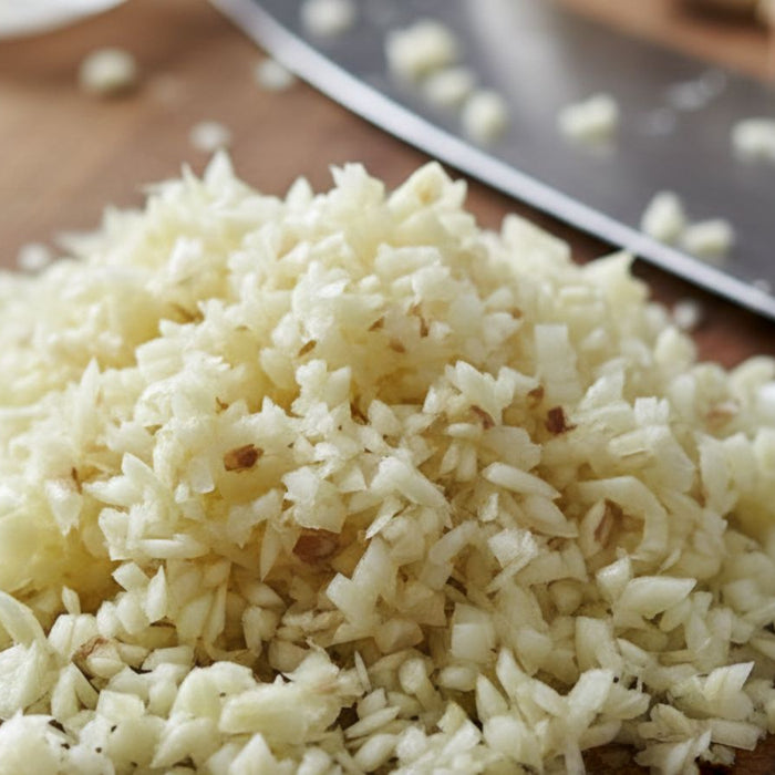 Finely chopped garlic on cutting board near metal kitchen knife