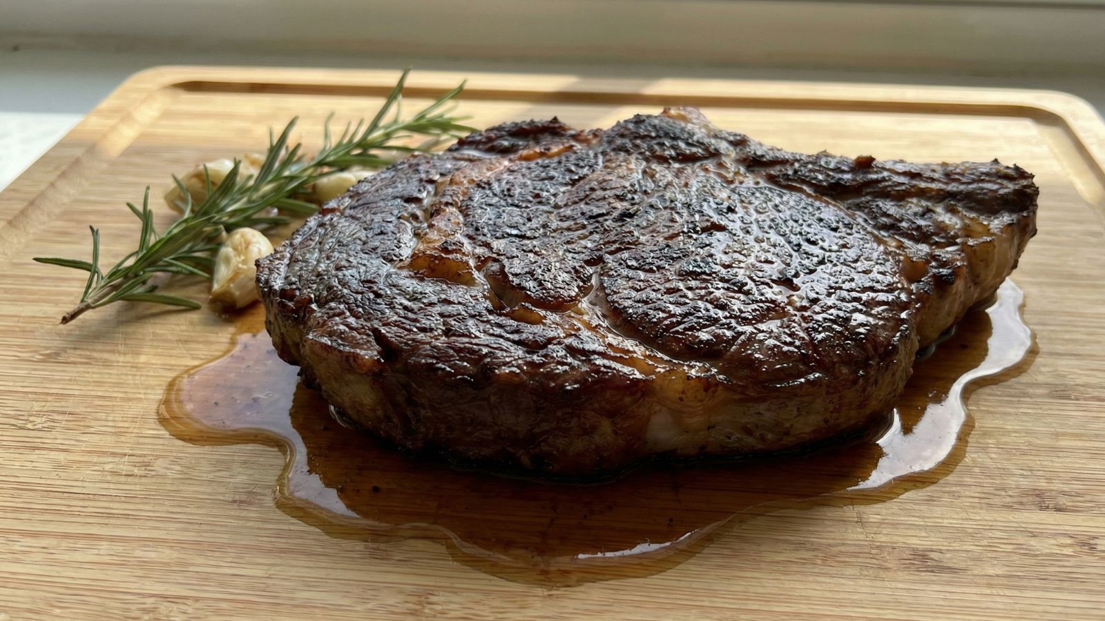 Seared ribeye steak resting with rosemary and garlic on board