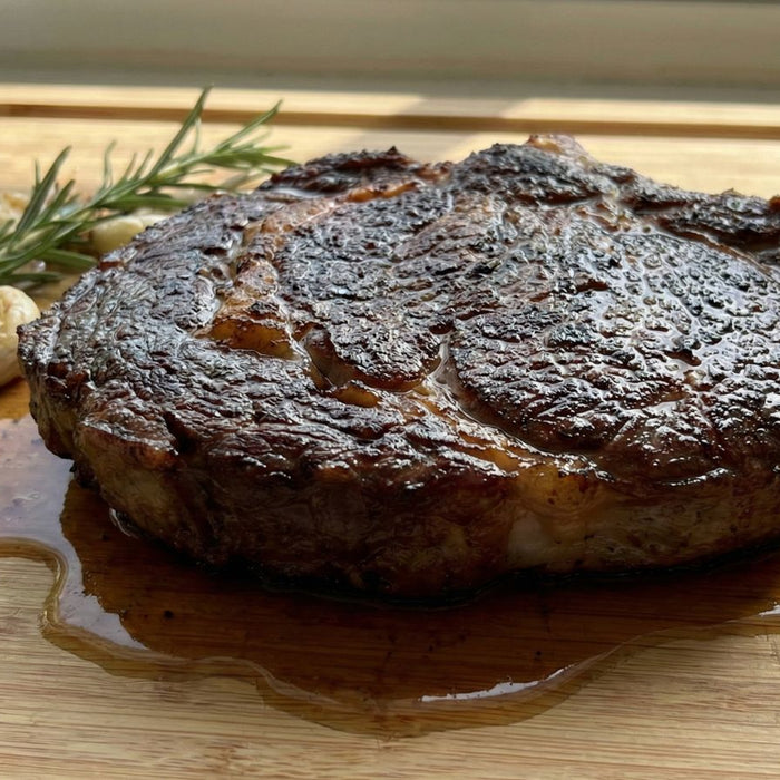 Seared ribeye steak resting with rosemary and garlic on board