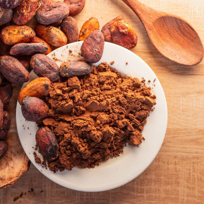 Cacao beans and cocoa powder on plate with wooden spoon