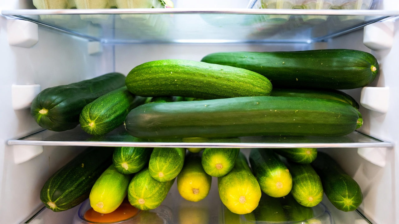 Many cucumbers packed on refrigerator shelves under cool white light.