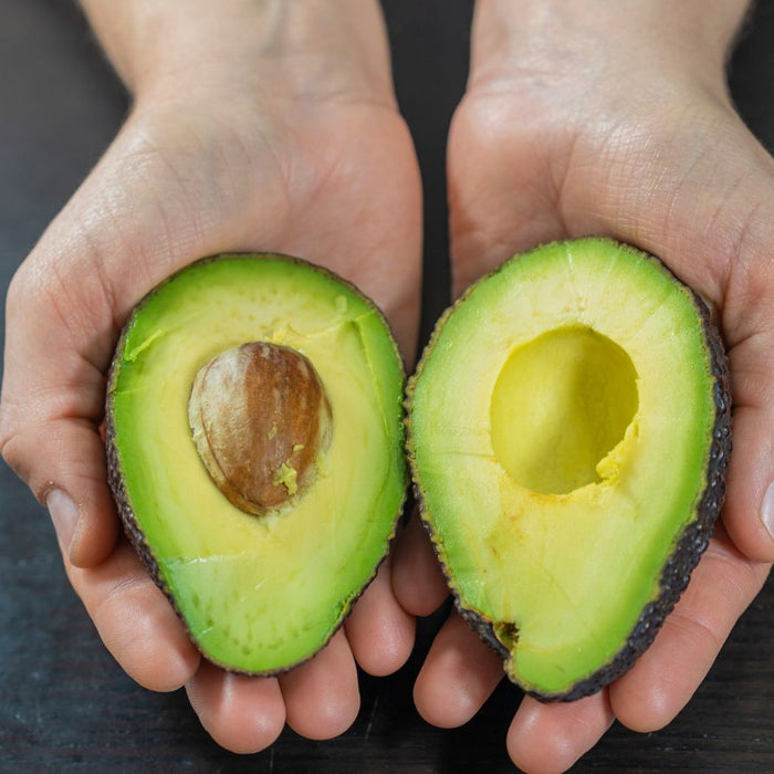 Hands holding avocado halves with seed on dark background