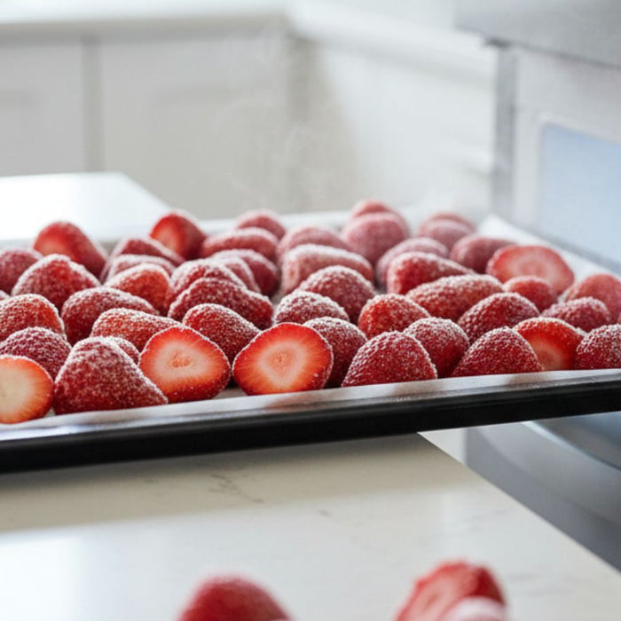 Tray of halved strawberries arranged for freezing inside a freezer
