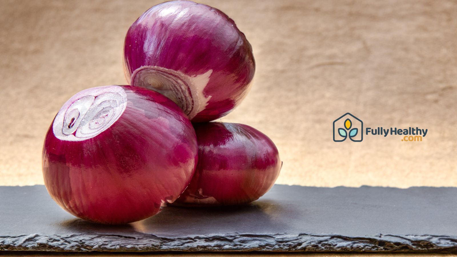 Whole red onions stacked on dark slate surface.