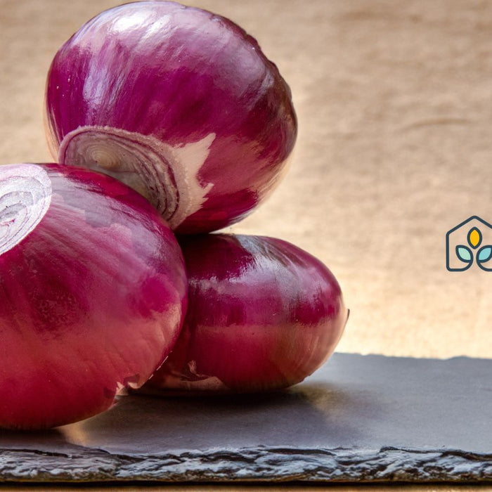 Whole red onions stacked on dark slate surface.