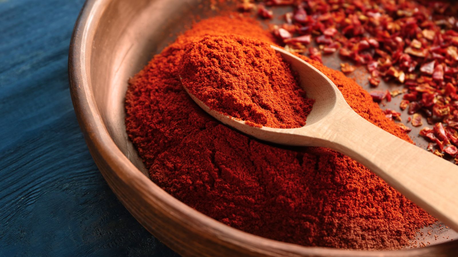 Wooden spoon resting in bowl filled with bright red paprika powder.