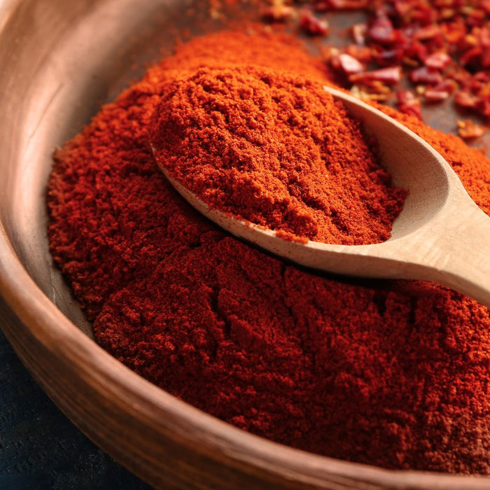 Wooden spoon resting in bowl filled with bright red paprika powder.