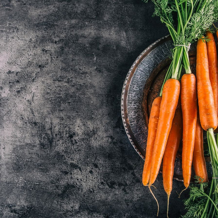 Fresh carrots with green tops on dark textured background