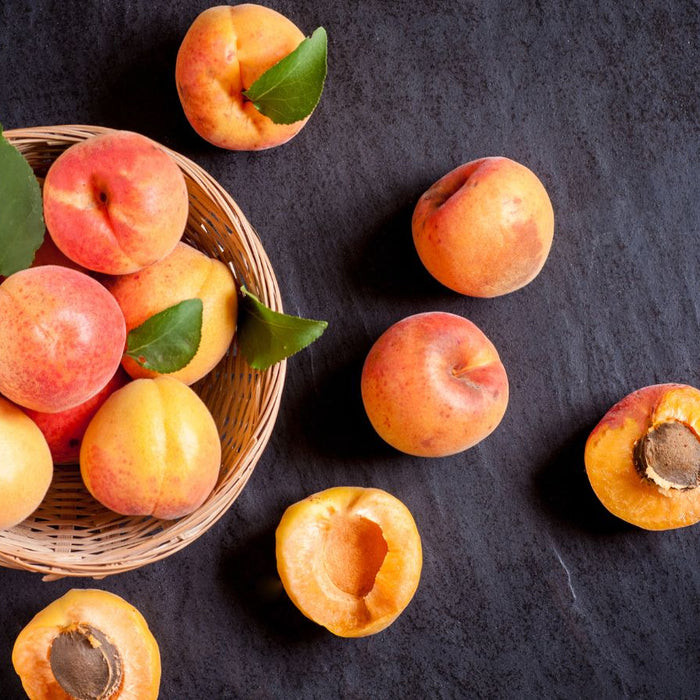 Basket of fresh apricots and halves on dark stone surface