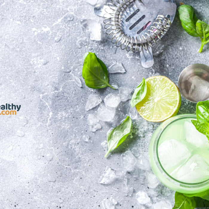 Basil lime cocktail with ice and herbs on gray stone background