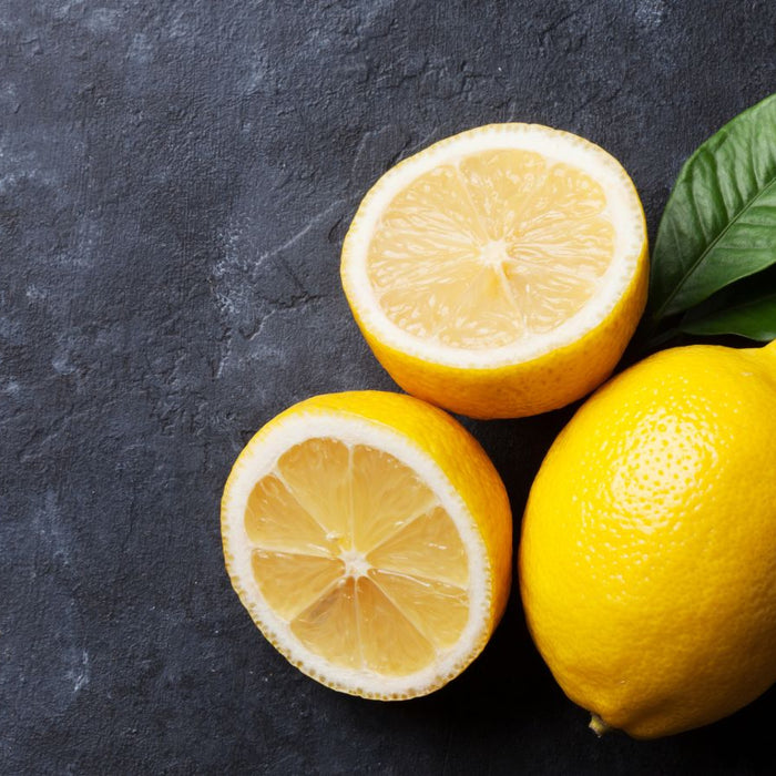 Whole and halved lemons with green leaves on dark surface