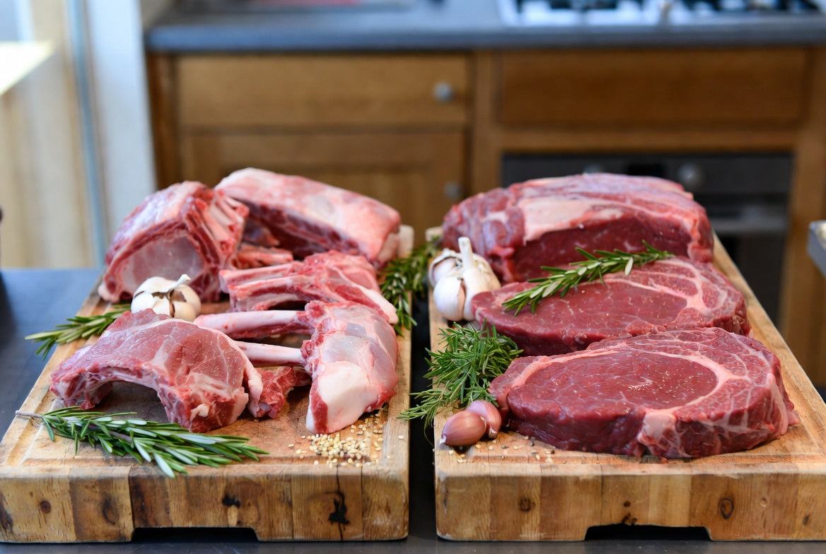Raw lamb chops and beef steaks compared on butcher block board