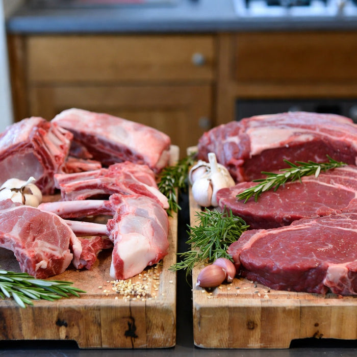 Raw lamb chops and beef steaks compared on butcher block board