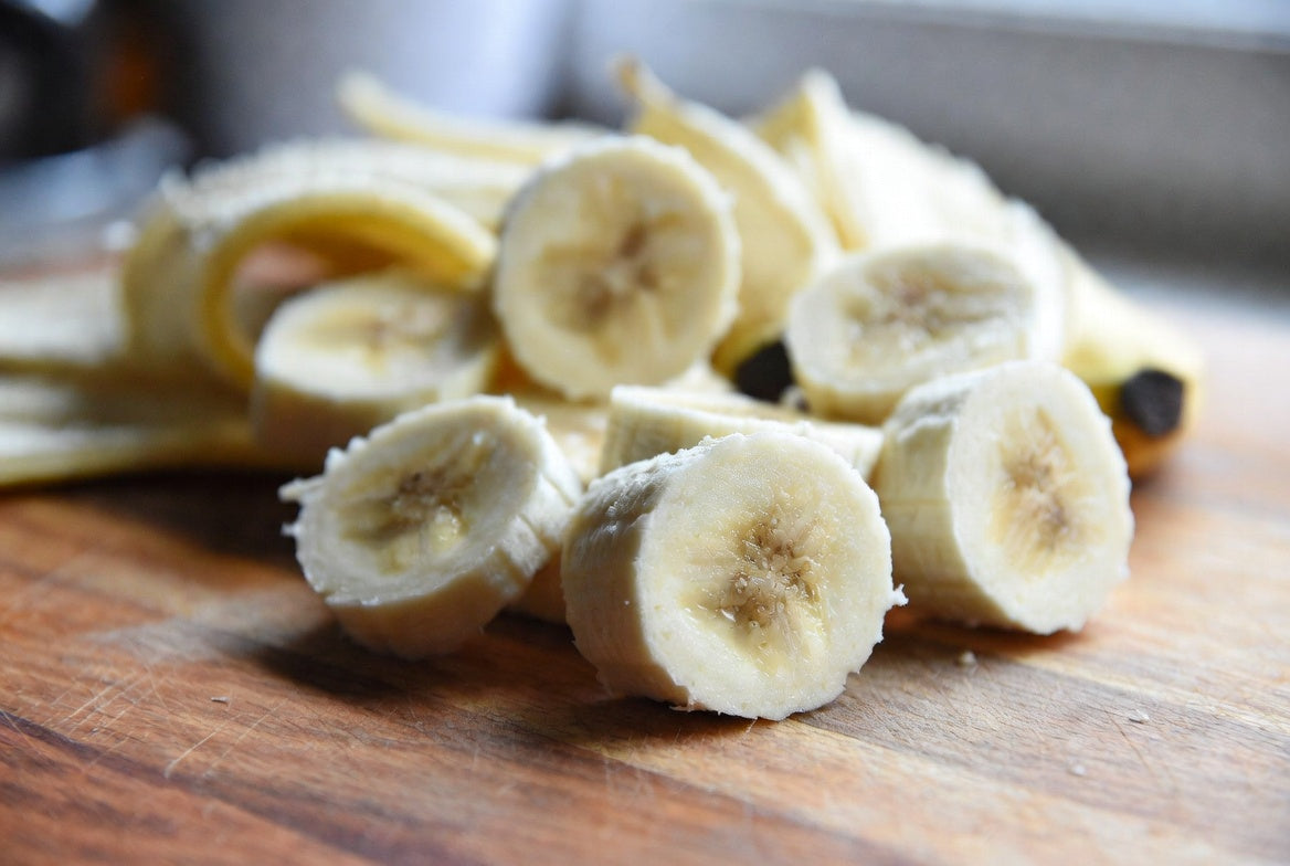 Close-up of sliced bananas on a cutting board with peel in background