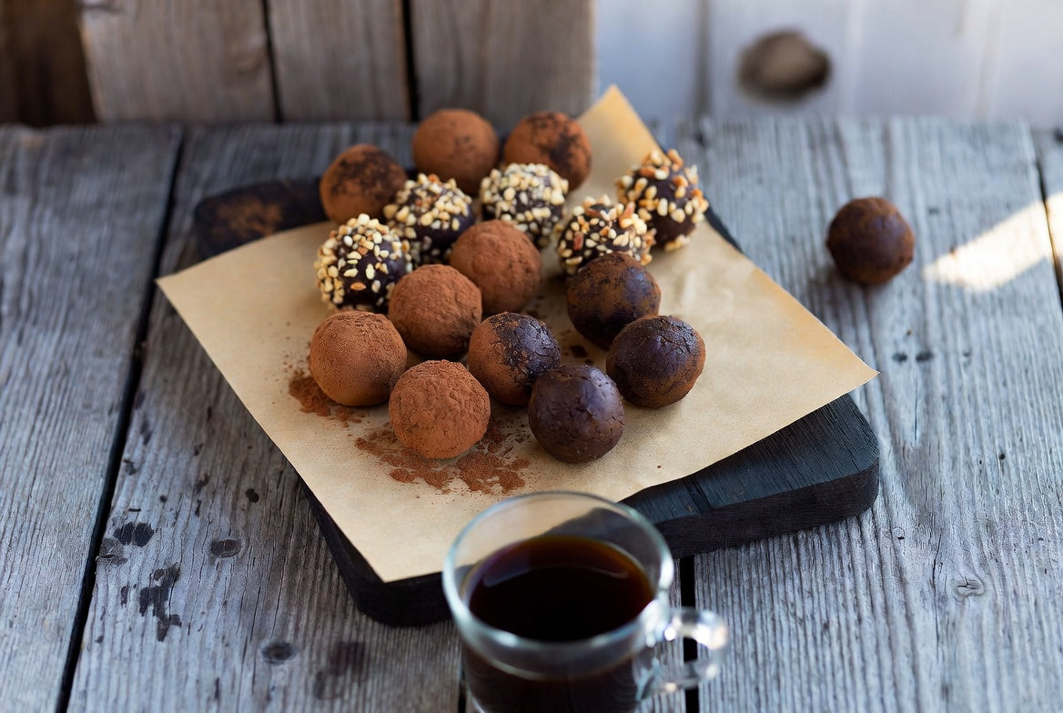 Assorted chocolate truffles on parchment beside a glass cup
