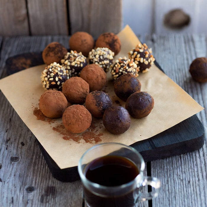 Assorted chocolate truffles on parchment beside a glass cup