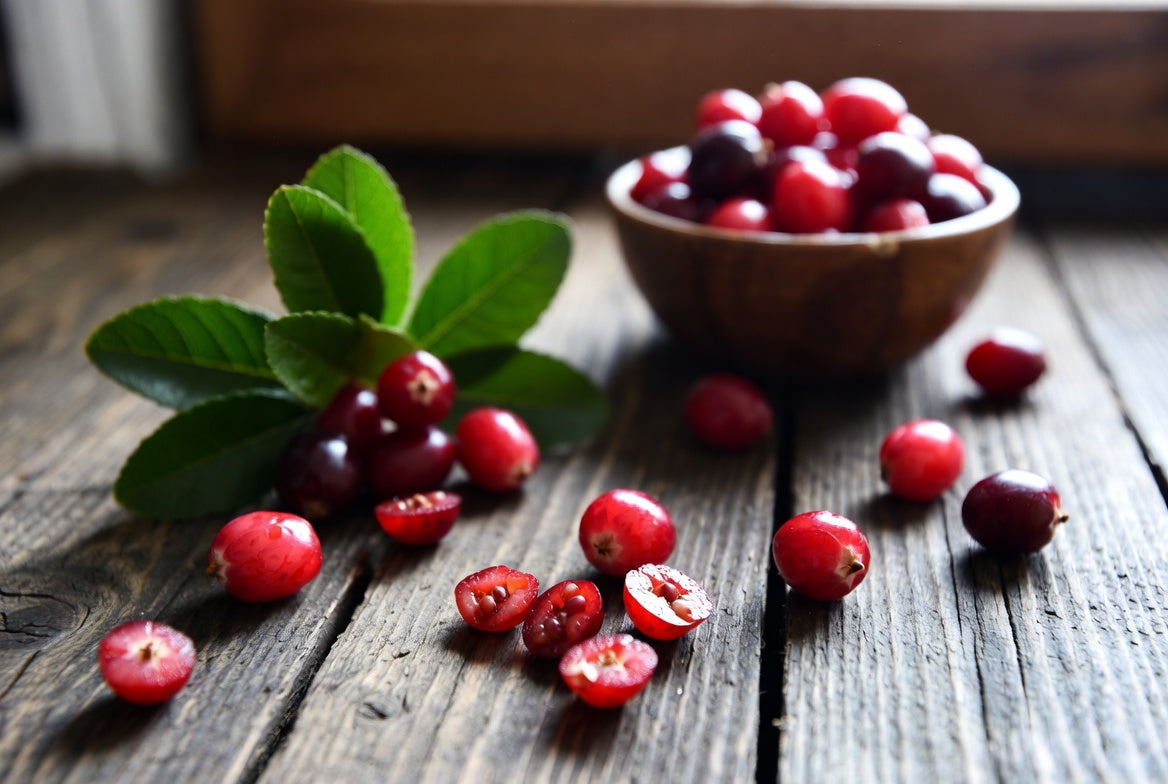 Fresh cranberries with leaves and sliced berries on rustic wood table
