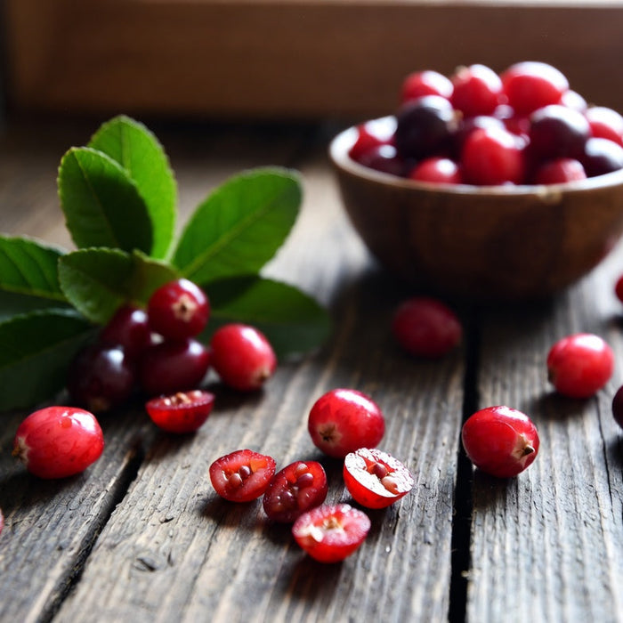 Fresh cranberries with leaves and sliced berries on rustic wood table