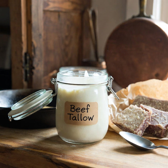 Jar of beef tallow on rustic counter beside skillet and raw beef cuts