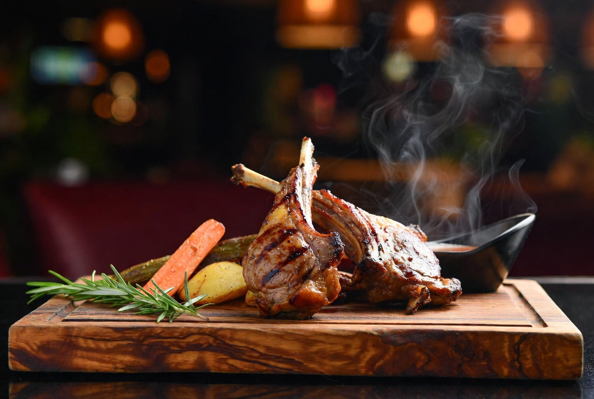Grilled lamb chops on wooden board with rosemary and vegetables