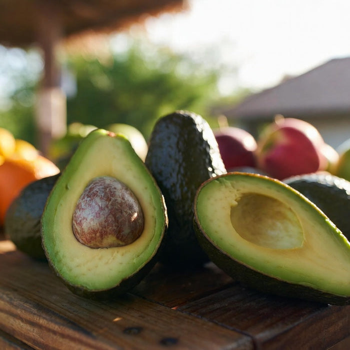 Fresh avocados cut open beside apples and oranges on a table