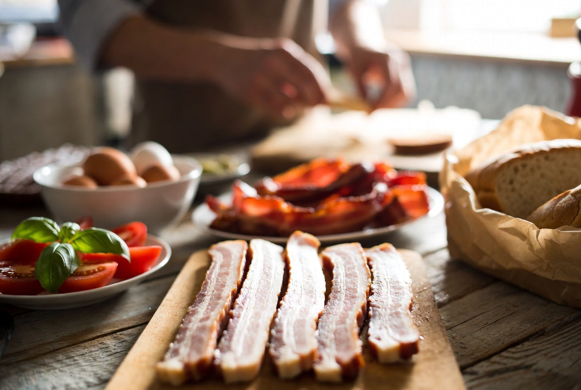 Raw bacon strips with breakfast ingredients on rustic kitchen counter