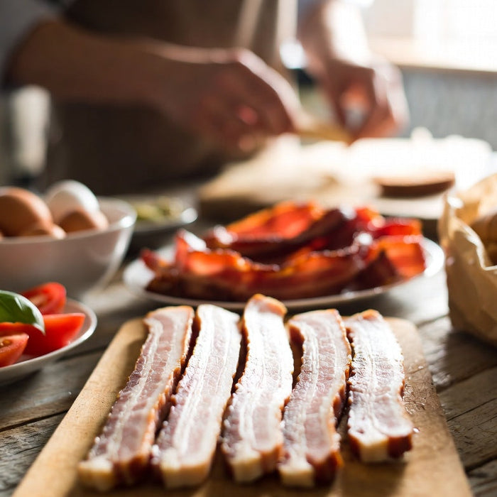 Raw bacon strips with breakfast ingredients on rustic kitchen counter
