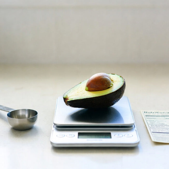 Halved avocado on a food scale with nutrition card nearby