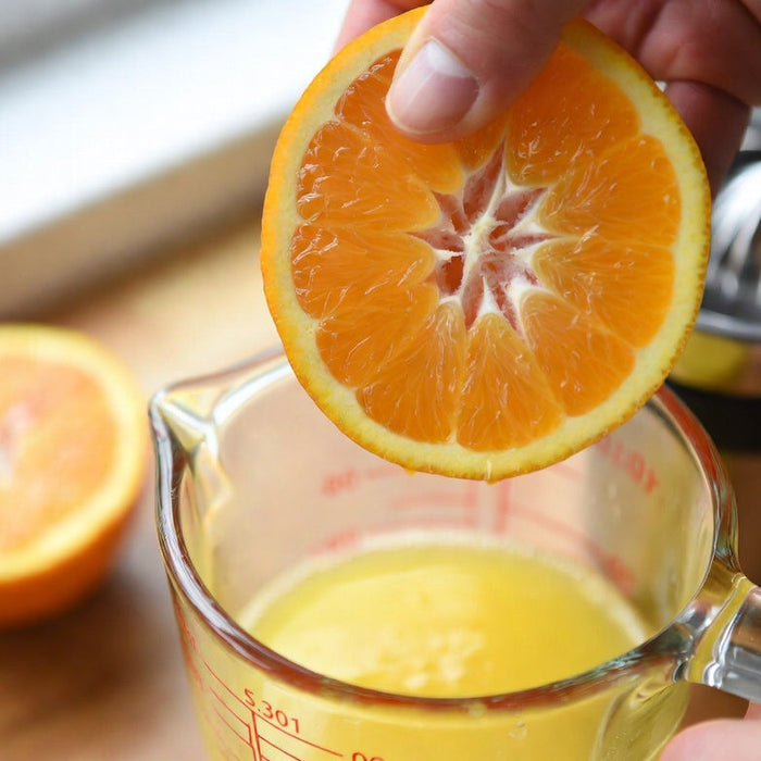 Fresh orange being squeezed into glass measuring cup