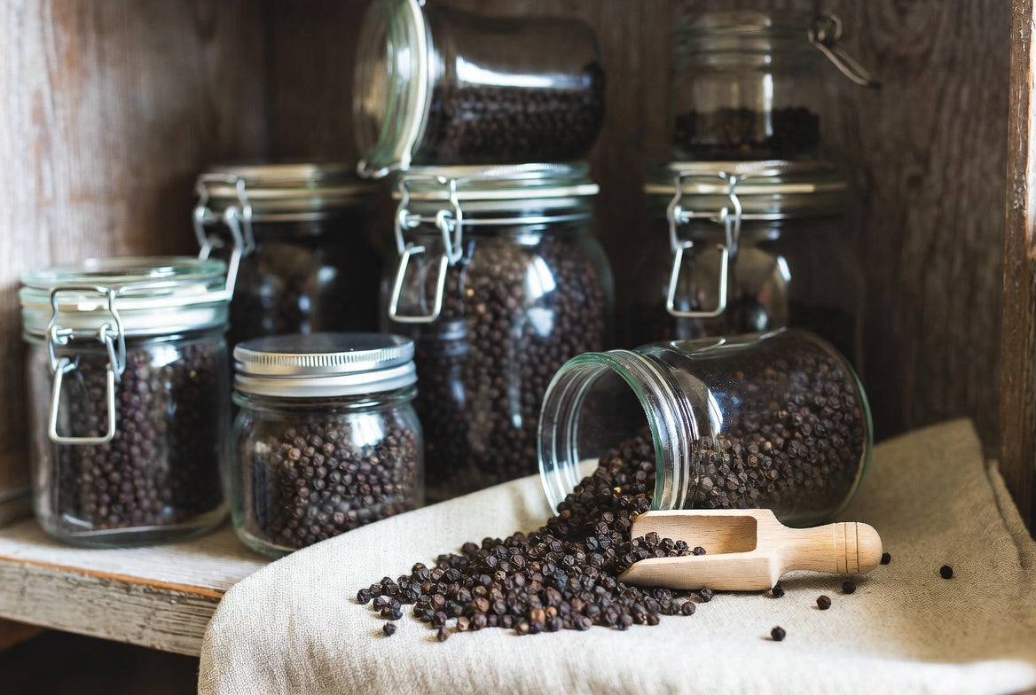 Glass jars filled with black peppercorns on rustic pantry shelf