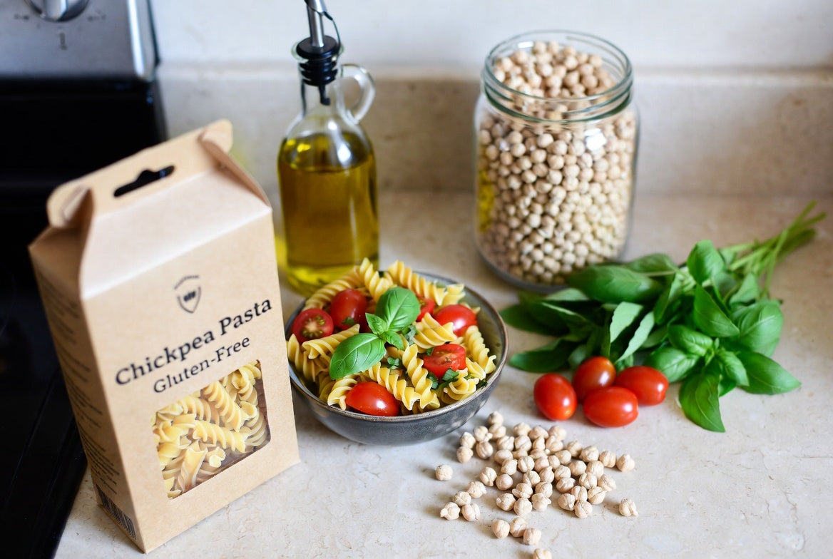 Chickpea pasta box with basil, tomatoes, and dry chickpeas on counter  Jars