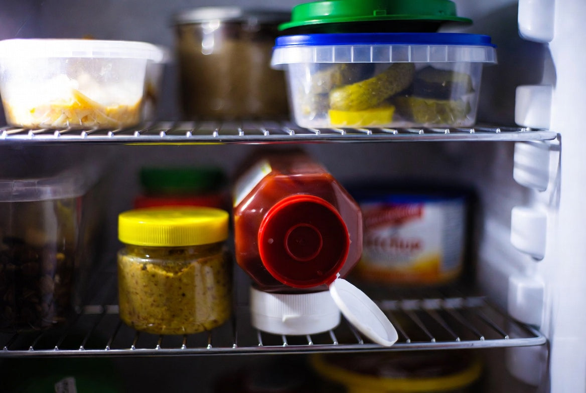 Open ketchup bottle stored beside mustard on refrigerator shelf