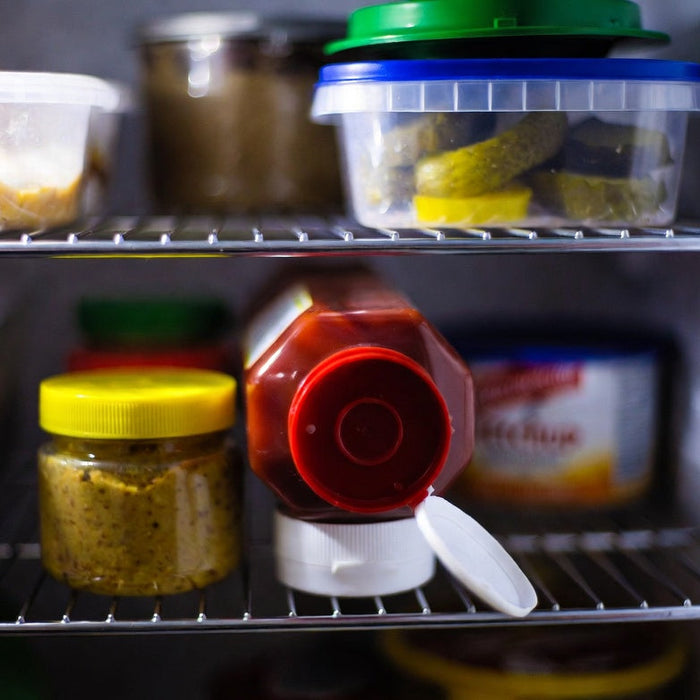 Open ketchup bottle stored beside mustard on refrigerator shelf