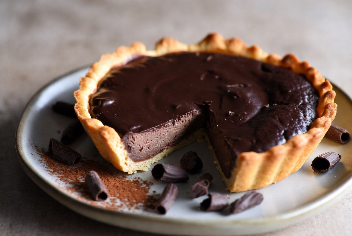 Chocolate tart with glossy filling and sliced piece on plate