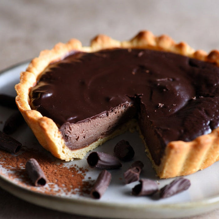 Chocolate tart with glossy filling and sliced piece on plate
