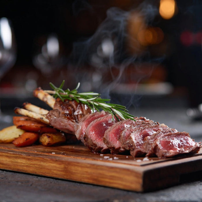 Medium-rare lamb rack sliced on board with rosemary and vegetables