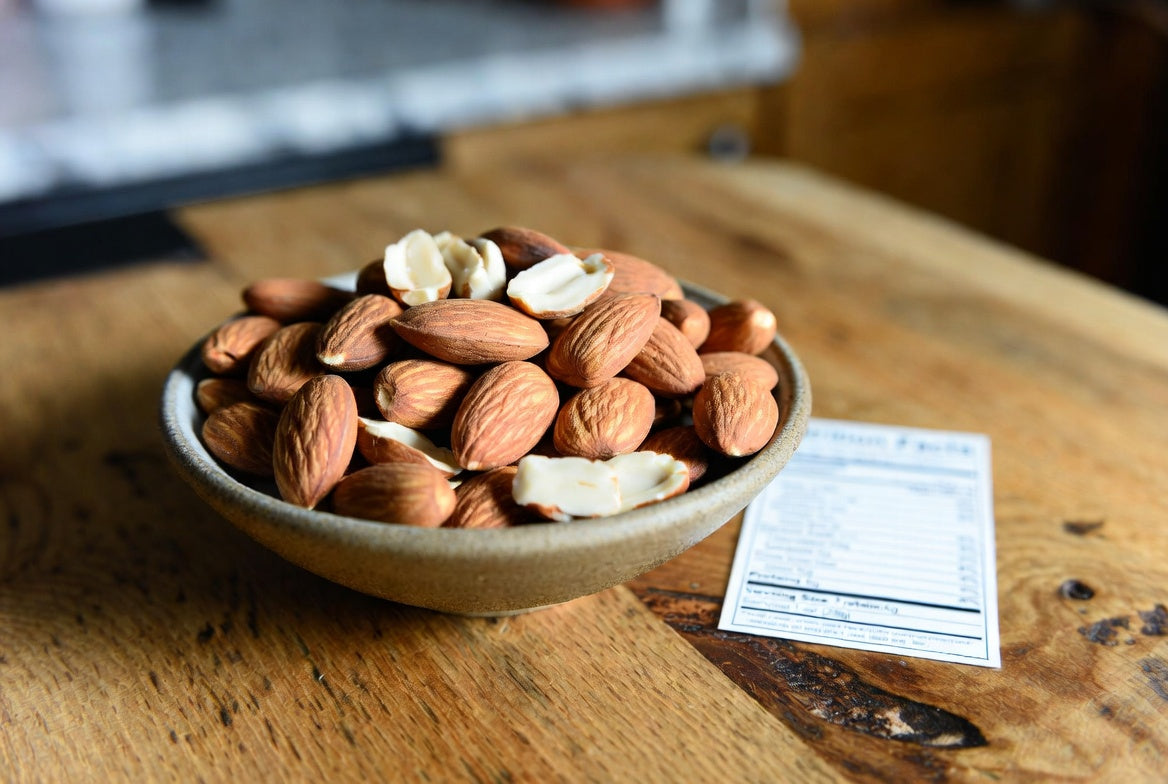 Bowl of almonds and peanut shells beside a nutrition facts card