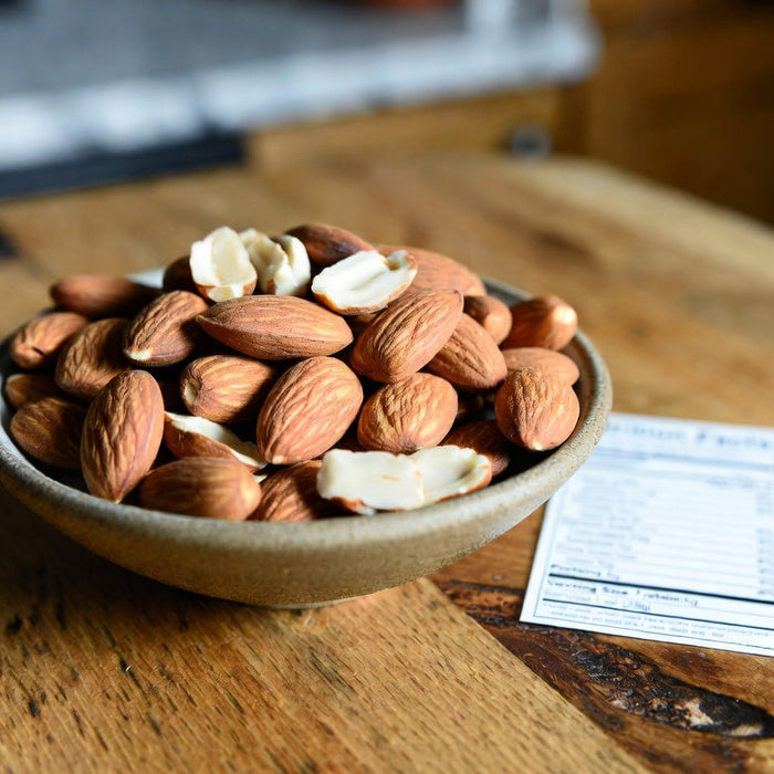 Bowl of almonds and peanut shells beside a nutrition facts card
