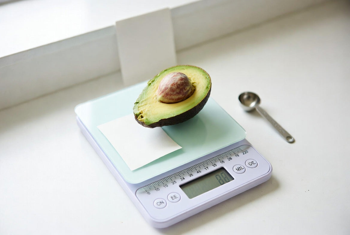 Half avocado on digital kitchen scale with measuring spoon nearby