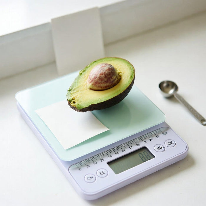 Half avocado on digital kitchen scale with measuring spoon nearby