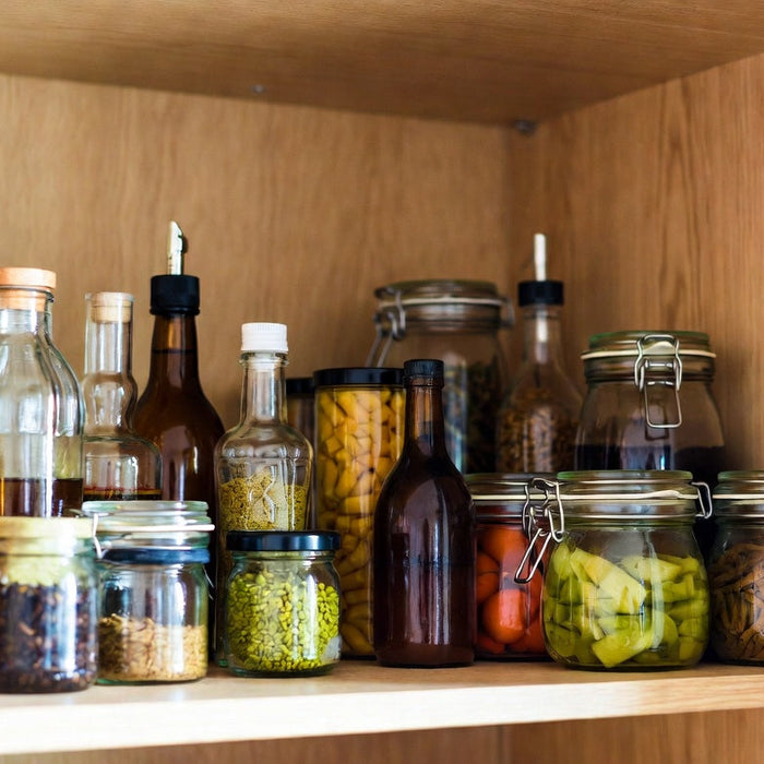 Pantry shelf with vinegar bottles, jars, and homemade preserved foods.
